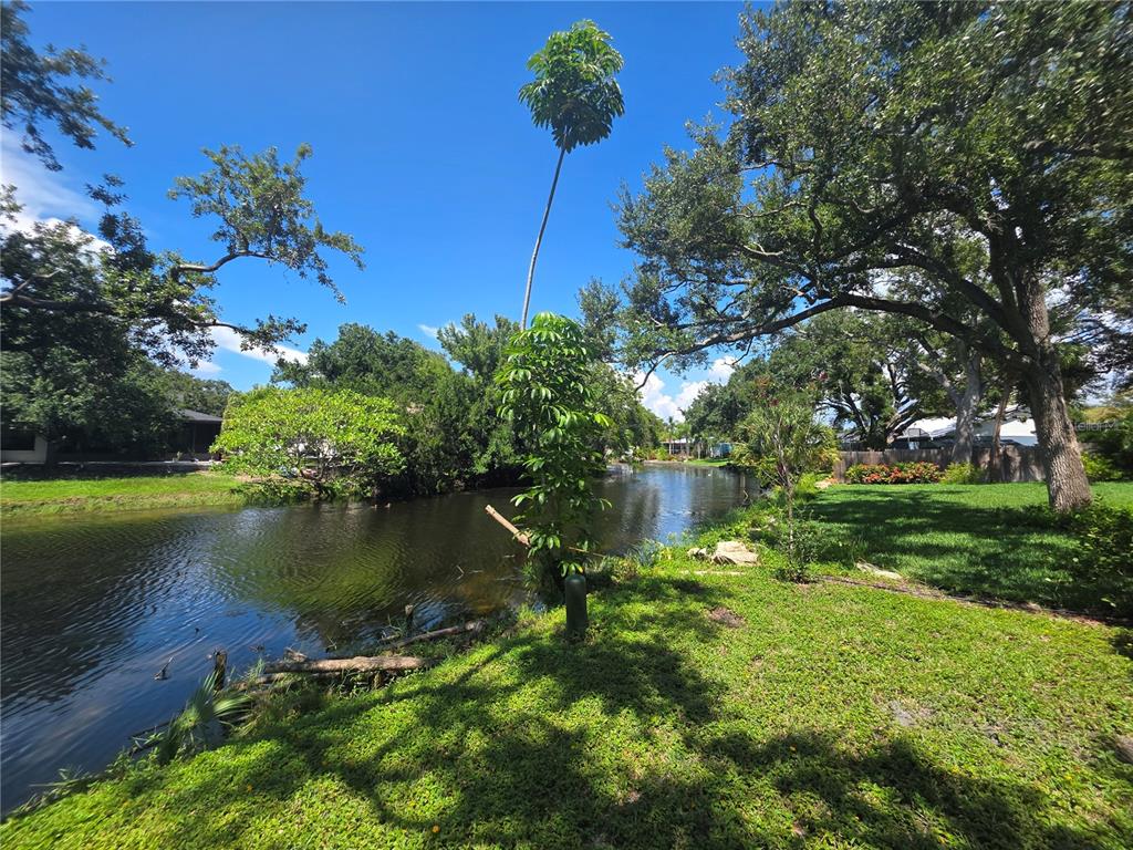 A grassy backyard overlooks a narrow canal lined with mature trees and lush vegetation — 7708 NW 9TH AVE DRIVE, BRADENTON, FL