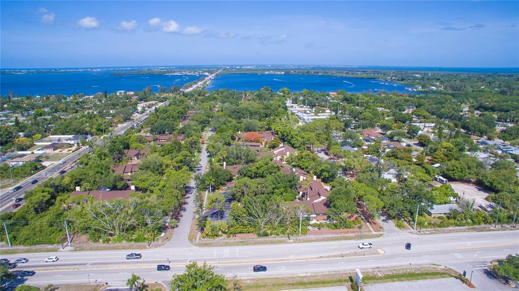 An aerial view shows a residential area with dense trees, buildings, and a nearby bay — 7708 NW 9TH AVE DRIVE, BRADENTON, FL