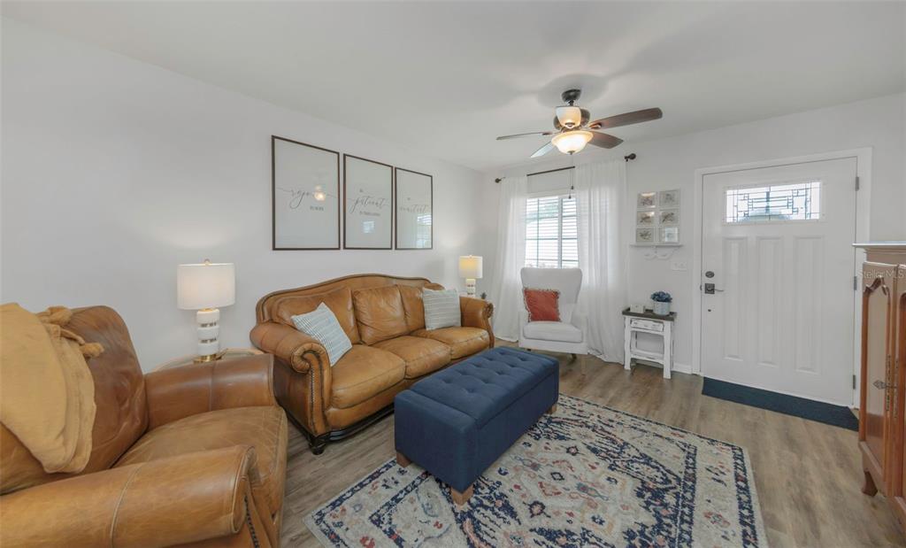 A living room features a leather sofa, a blue ottoman, and a white front door — 9919 TULIP STREET N, PINELLAS PARK, FL