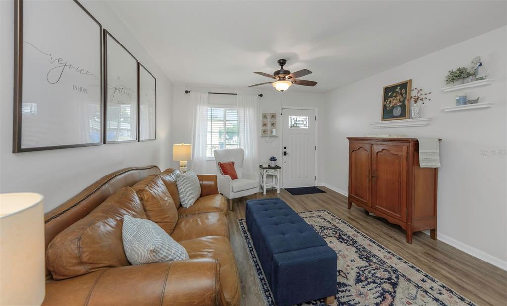 A living room features a brown leather sofa, a blue ottoman, and a wooden cabinet — 9919 TULIP STREET N, PINELLAS PARK, FL