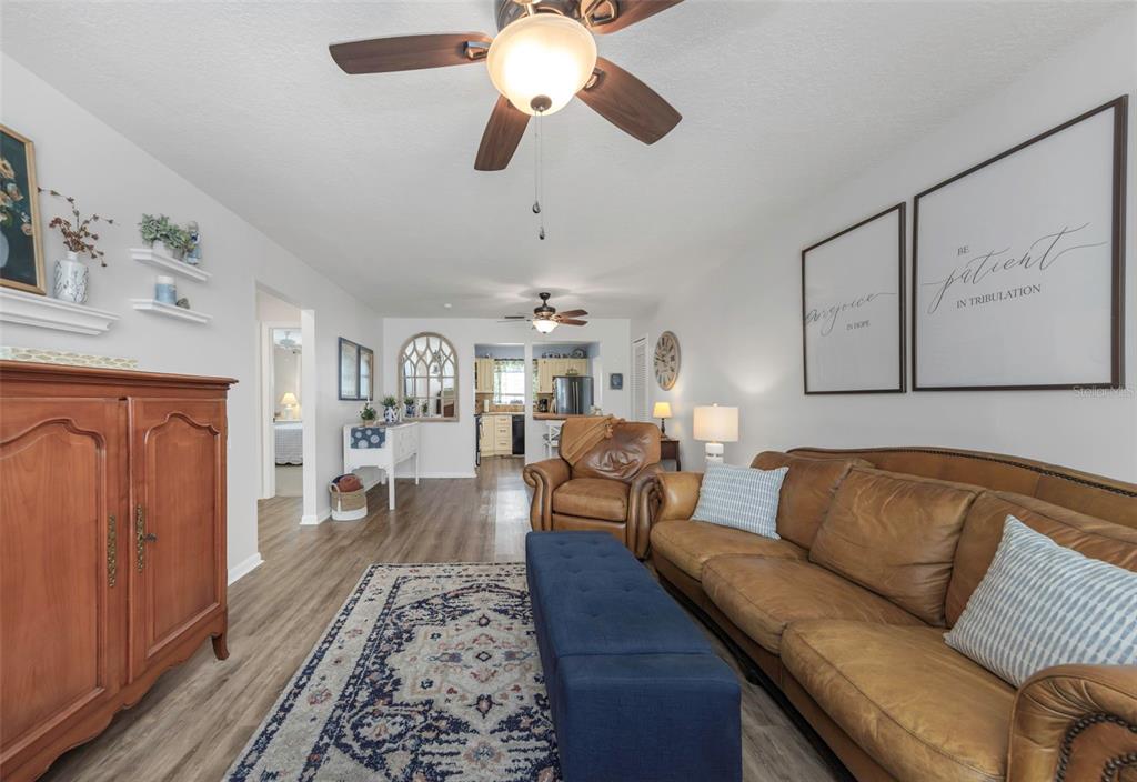 A living room features a leather sofa, blue ottoman, wood-look flooring, and a ceiling fan — 9919 TULIP STREET N, PINELLAS PARK, FL
