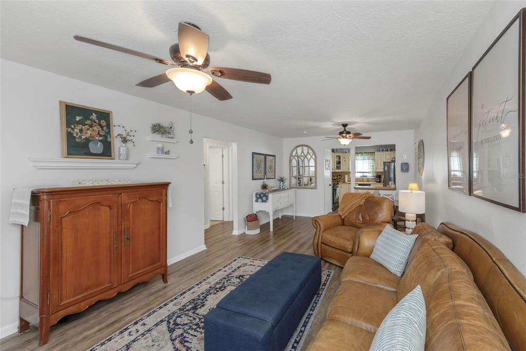 A living room features wood-look flooring, a brown leather sofa, and a wooden cabinet — 9919 TULIP STREET N, PINELLAS PARK, FL