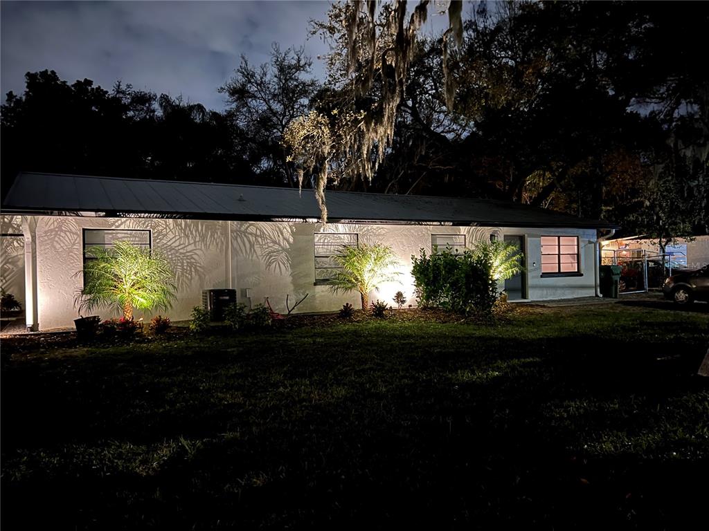 A single-story white house at night with illuminated landscaping and palm trees in the front yard — 1840 3RD AVENUE E, BRADENTON, FL