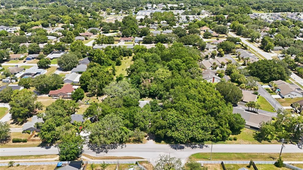 An aerial view shows a wooded lot surrounded by residential houses and a paved road — 2675 E WASHINGTON AVENUE, EUSTIS, FL