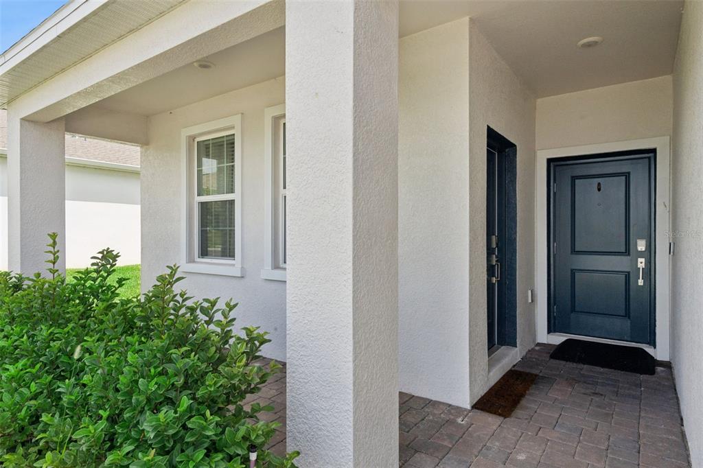 A covered entryway features a dark blue front door, white stucco walls, and paver flooring — 4511 HILLINGDAM ROAD, DAVENPORT, FL