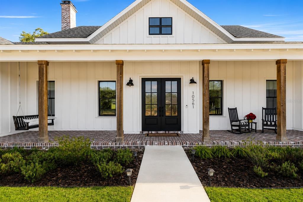 A white farmhouse with a brick porch, wooden columns, and a black double front door — 10561 NE 104TH CIRCLE, OXFORD, FL