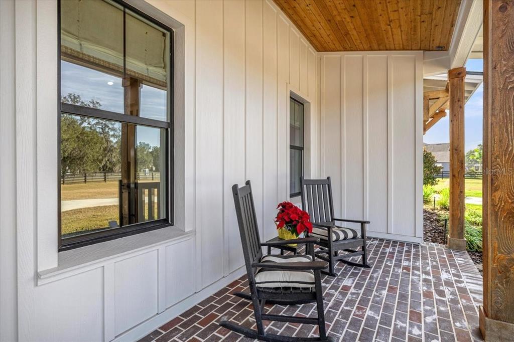 A covered porch features a brick floor, white board-and-batten siding, and two black rocking chairs — 10561 NE 104TH CIRCLE, OXFORD, FL