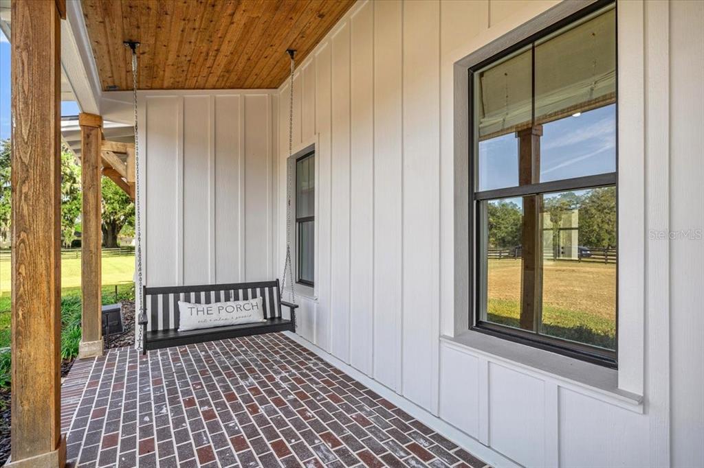 A covered porch features a brick floor, white board-and-batten siding, and a black hanging bench — 10561 NE 104TH CIRCLE, OXFORD, FL