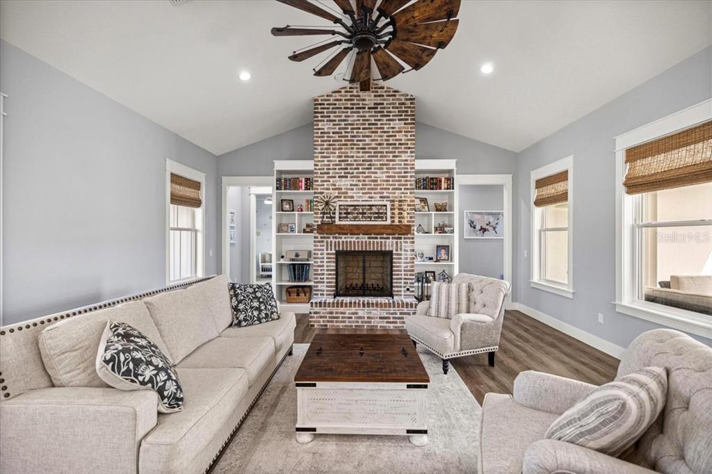 A living room features a brick fireplace, built-in bookshelves, a windmill ceiling fan, and furniture — 10561 NE 104TH CIRCLE, OXFORD, FL