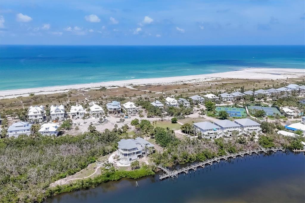 An aerial view shows coastal homes, a wooden dock, and tennis courts near the beach — 7365 PALM ISLAND DRIVE, PLACIDA, FL