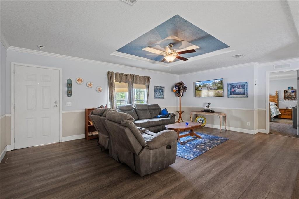 A living room features gray sofas, a blue-accented tray ceiling, and wood-look flooring — 87 NE 544TH STREET, OLD TOWN, FL