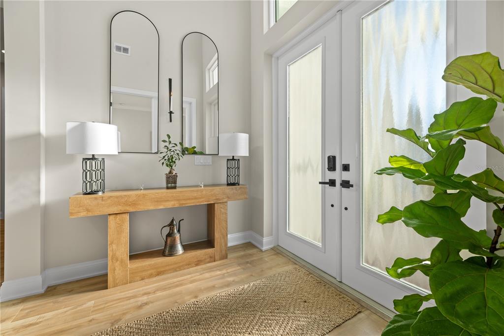 A modern entryway features a wooden console table, two arched mirrors, and double glass doors — 2559 PALM AVENUE, FLAGLER BEACH, FL