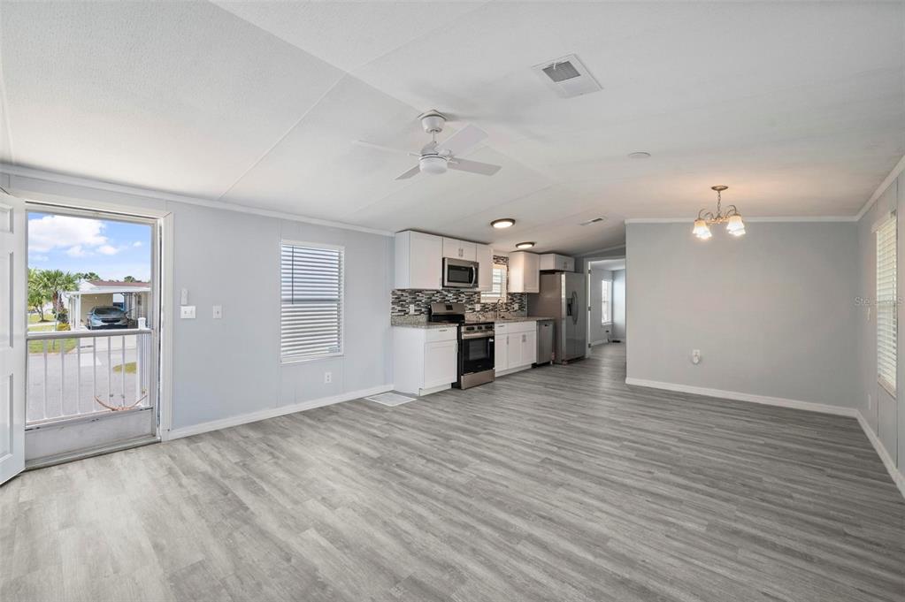 An open-concept kitchen and living area features light gray walls, wood-look flooring, and white cabinetry — 1000 KINGS HIGHWAY UNIT 101, PORT CHARLOTTE, FL