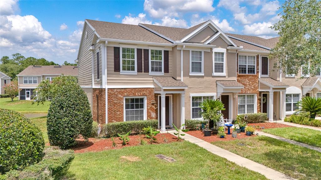 A two-story townhouse with tan siding, brick accents, and a shingled roof under a cloudy sky — 6544 ARCHING BRANCH CIRCLE, JACKSONVILLE, FL