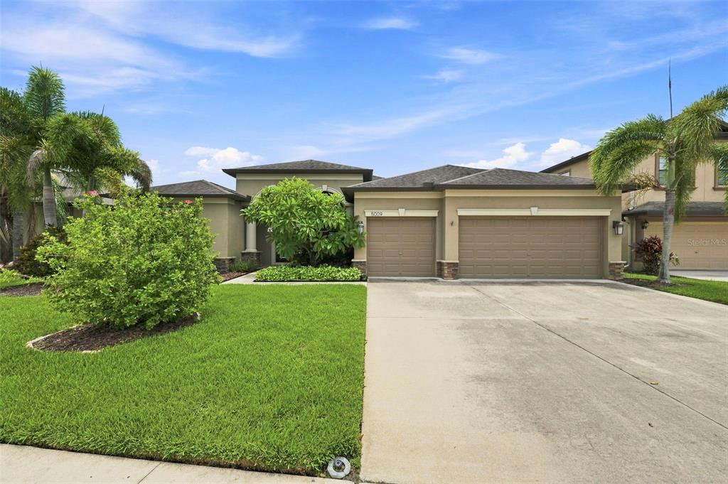 A single-story house with a three-car garage, palm trees, and a landscaped front lawn — 5009 JAGGED CLOUD DRIVE, WIMAUMA, FL