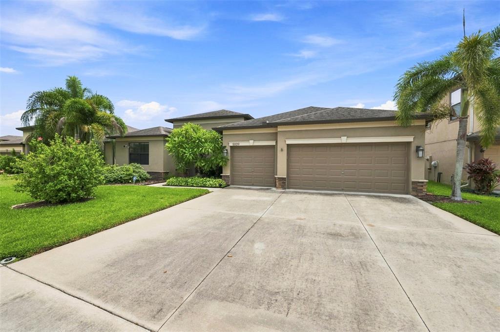 A single-story house with a three-car garage, beige stucco exterior, and a concrete driveway — 5009 JAGGED CLOUD DRIVE, WIMAUMA, FL