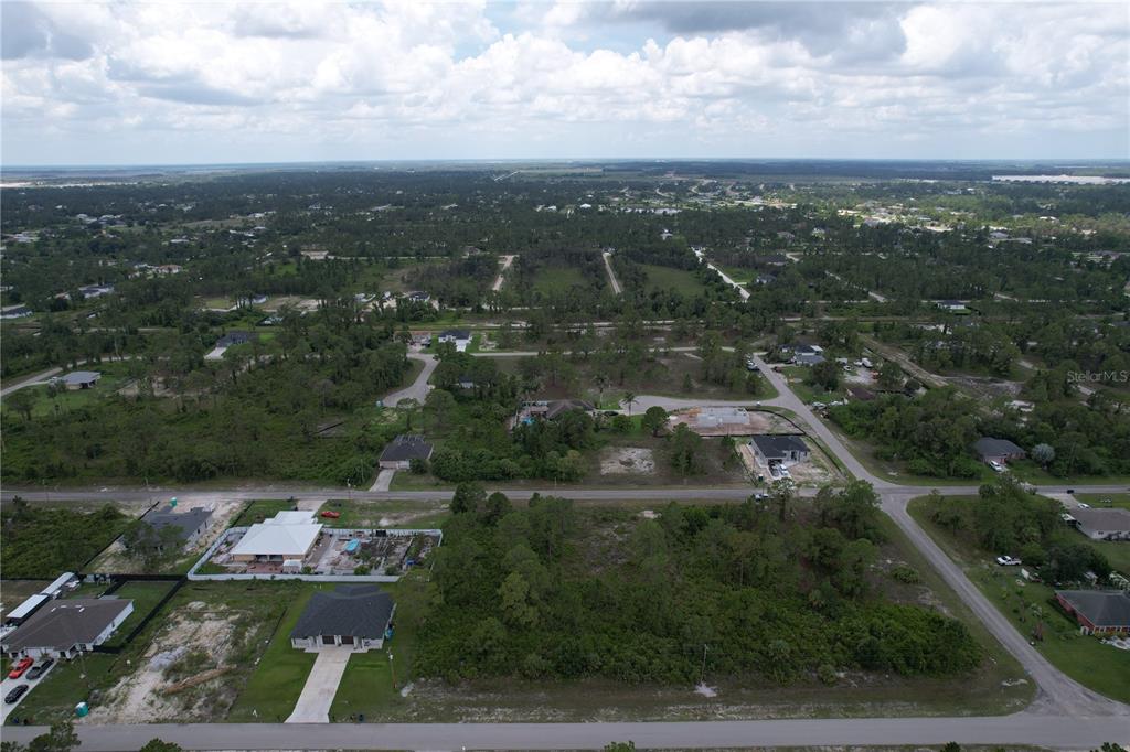 An aerial view shows a residential neighborhood with scattered houses and undeveloped wooded lots — 1056 JAGUAR BOULEVARD, LEHIGH ACRES, FL