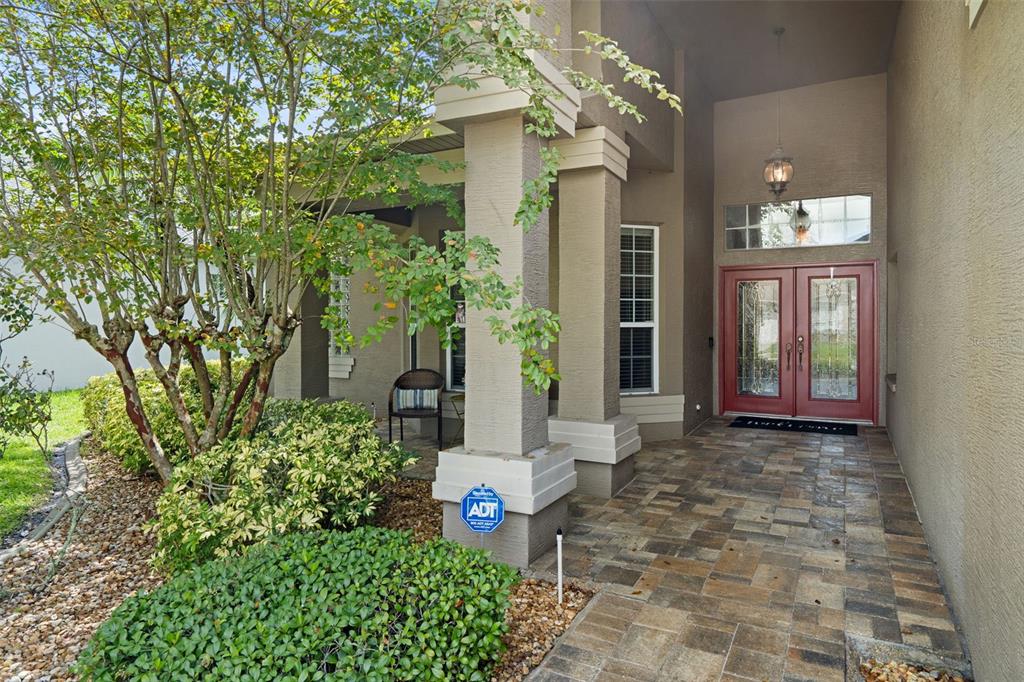 A covered entryway with a stone-tiled porch, red double doors, and a small sitting area — 2313 EDELWEISS LOOP, TRINITY, FL