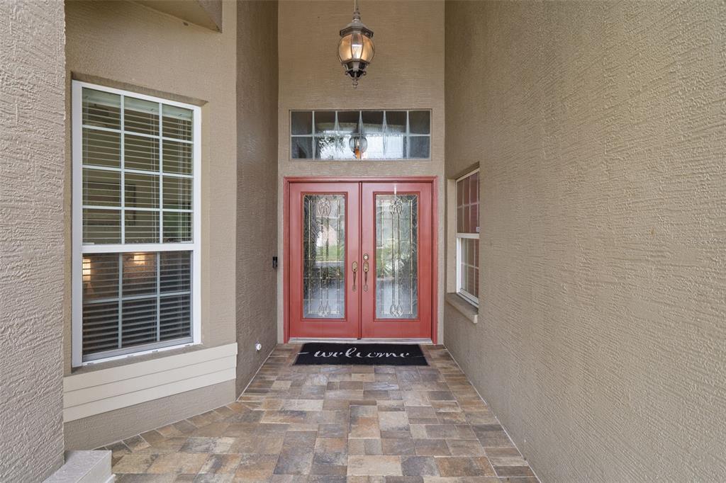 A covered entryway features a red double door, tiled flooring, and a hanging light fixture — 2313 EDELWEISS LOOP, TRINITY, FL