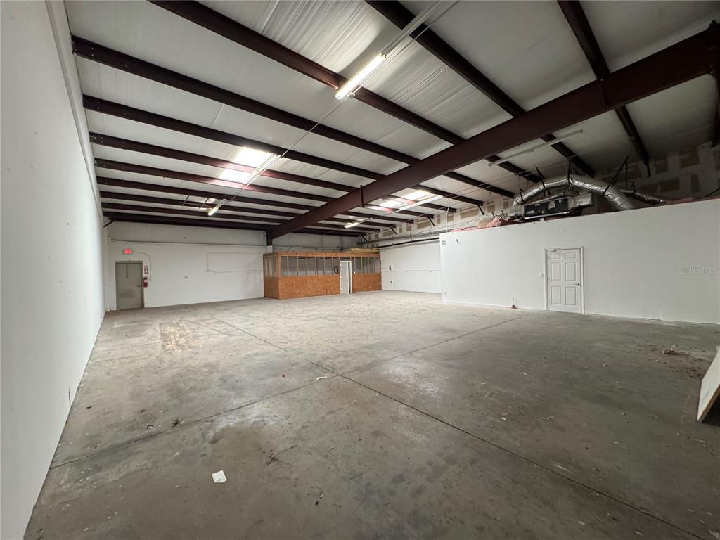 An open industrial warehouse space features a concrete floor, exposed ceiling beams, and a partition — 1408 HAMLIN AVENUE UNIT D, ST CLOUD, FL