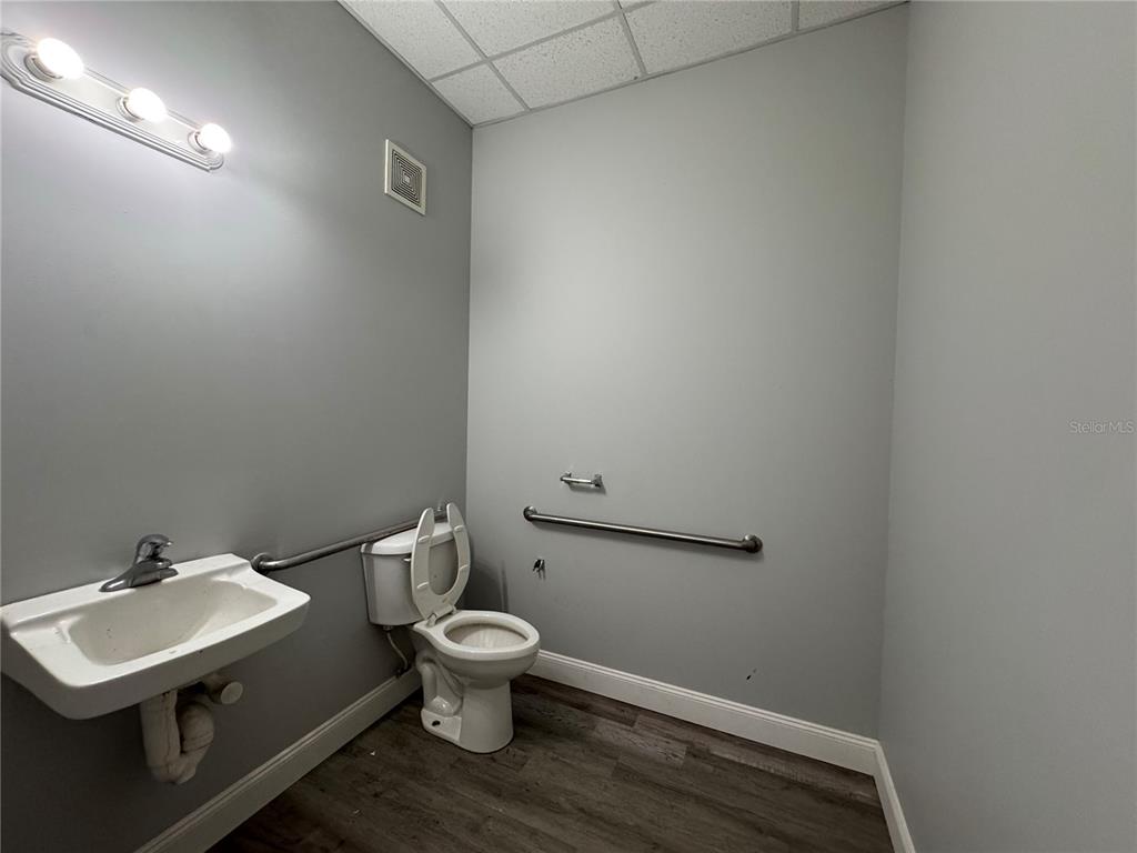 A small, gray-walled restroom features a wall-mounted sink, a toilet, and a grab bar — 1408 HAMLIN AVENUE UNIT D, ST CLOUD, FL