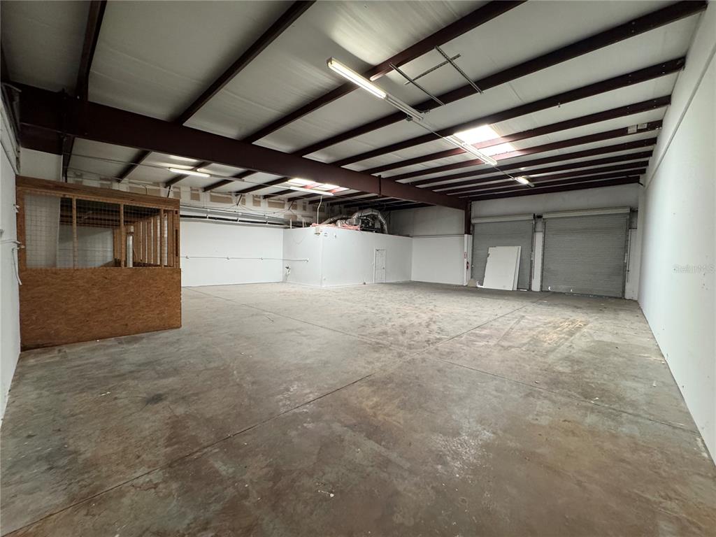 An empty warehouse space features a concrete floor, metal roll-up doors, and a wooden stall — 1408 HAMLIN AVENUE UNIT D, ST CLOUD, FL