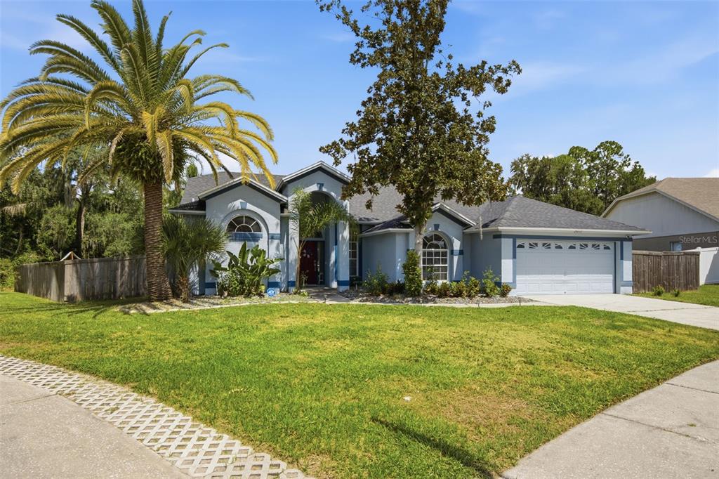A single-story blue house with a palm tree, a large tree, and a two-car garage — 28707 RALEIGH PLACE, WESLEY CHAPEL, FL