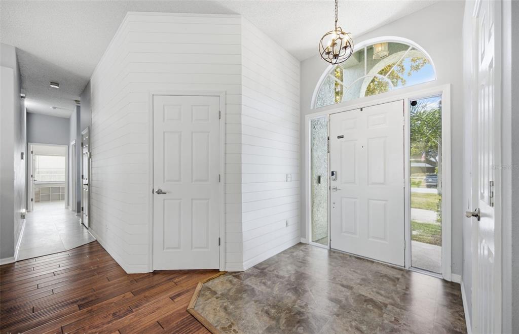 An entryway features a white shiplap wall, tile flooring, a front door, and wood flooring — 28707 RALEIGH PLACE, WESLEY CHAPEL, FL