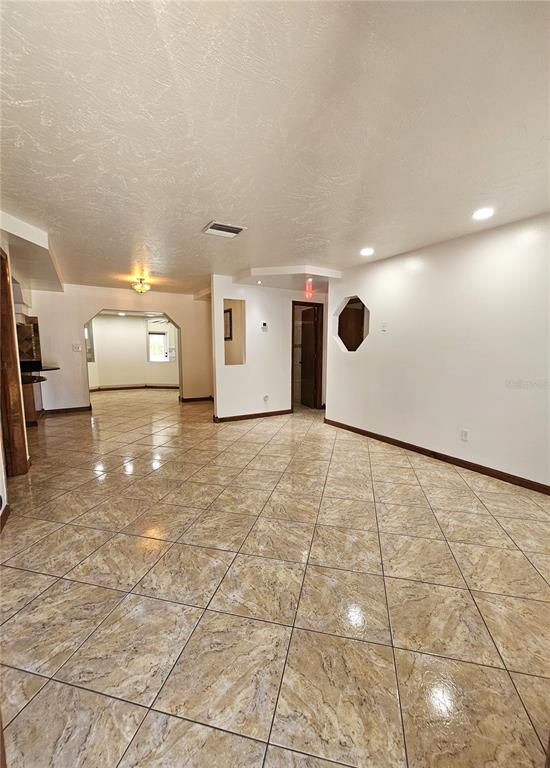 An open-concept room features light-colored tile flooring, white walls, and a unique octagonal wall cutout — 3709 WESTGATE ROAD, ORLANDO, FL