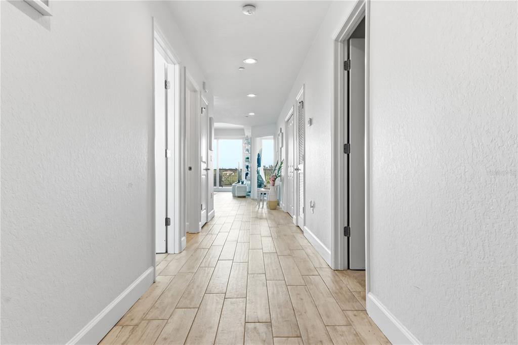 A long hallway with light wood-look tile flooring leads toward a bright room with windows — 19519 GULF BOULEVARD UNIT 403, INDIAN SHORES, FL