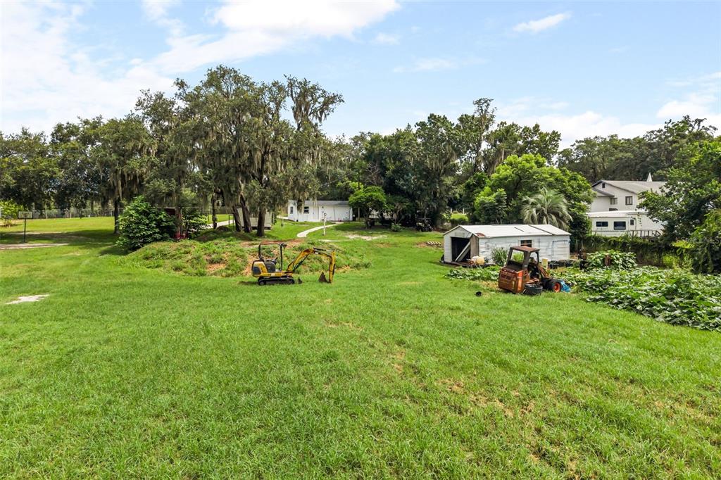 A grassy lot features a small excavator, a shed, and a house in the background — 250 LONGWOOD HILLS ROAD, LONGWOOD, FL