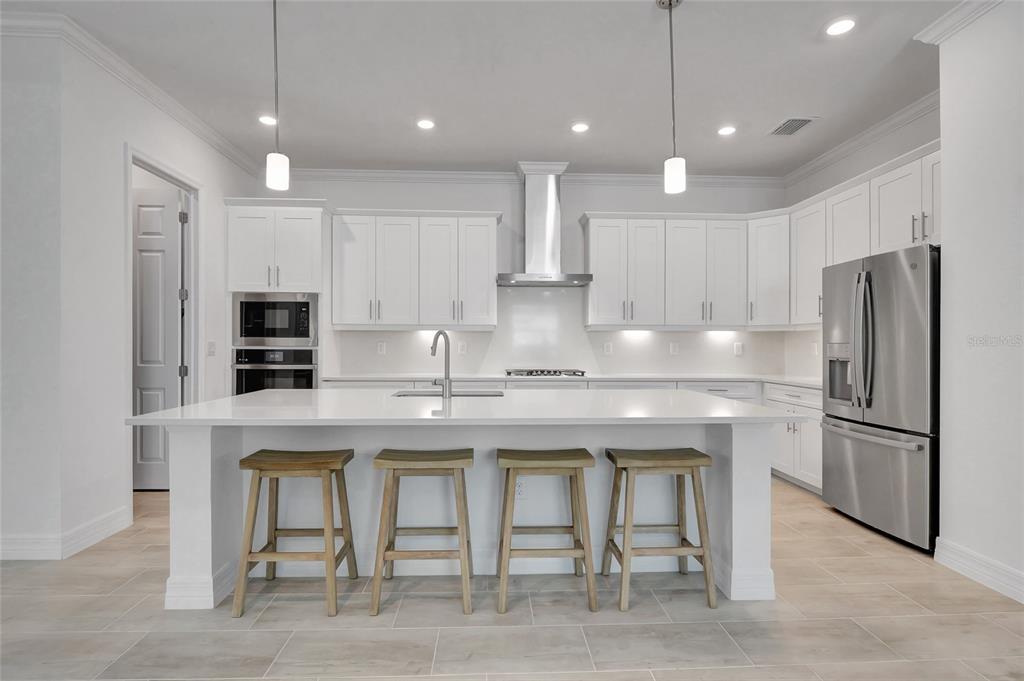 A modern white kitchen features a large island with four wooden stools and stainless appliances — 14257 BLUE BAY CIRCLE, FORT MYERS, FL