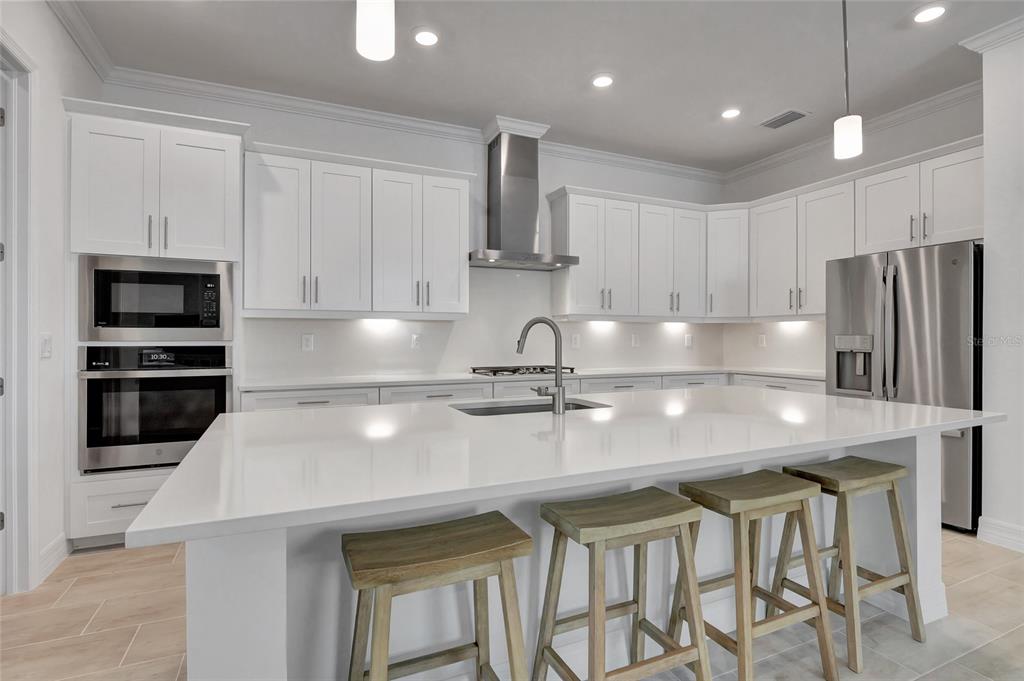 A modern kitchen features white cabinetry, a large quartz island, stainless steel appliances, and barstools — 14257 BLUE BAY CIRCLE, FORT MYERS, FL