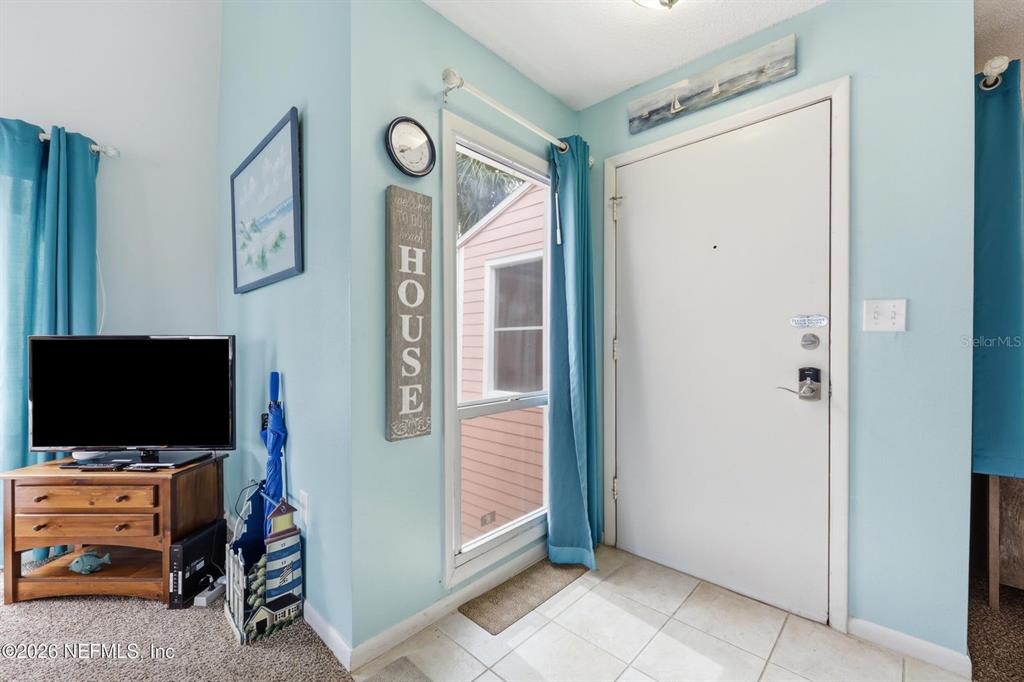 An entryway with light blue walls, a white front door, tile flooring, and a television stand — 6300 A1A S UNIT A92U, ST AUGUSTINE, FL