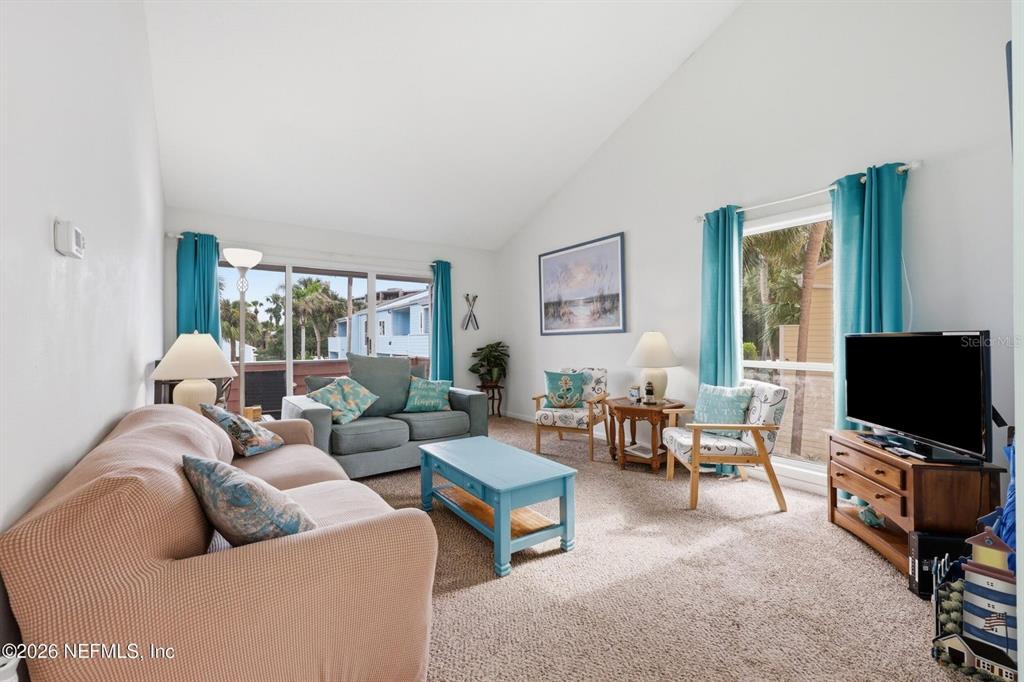 A living room features a vaulted ceiling, beige sofa, blue coffee table, and sliding glass doors — 6300 A1A S UNIT A92U, ST AUGUSTINE, FL