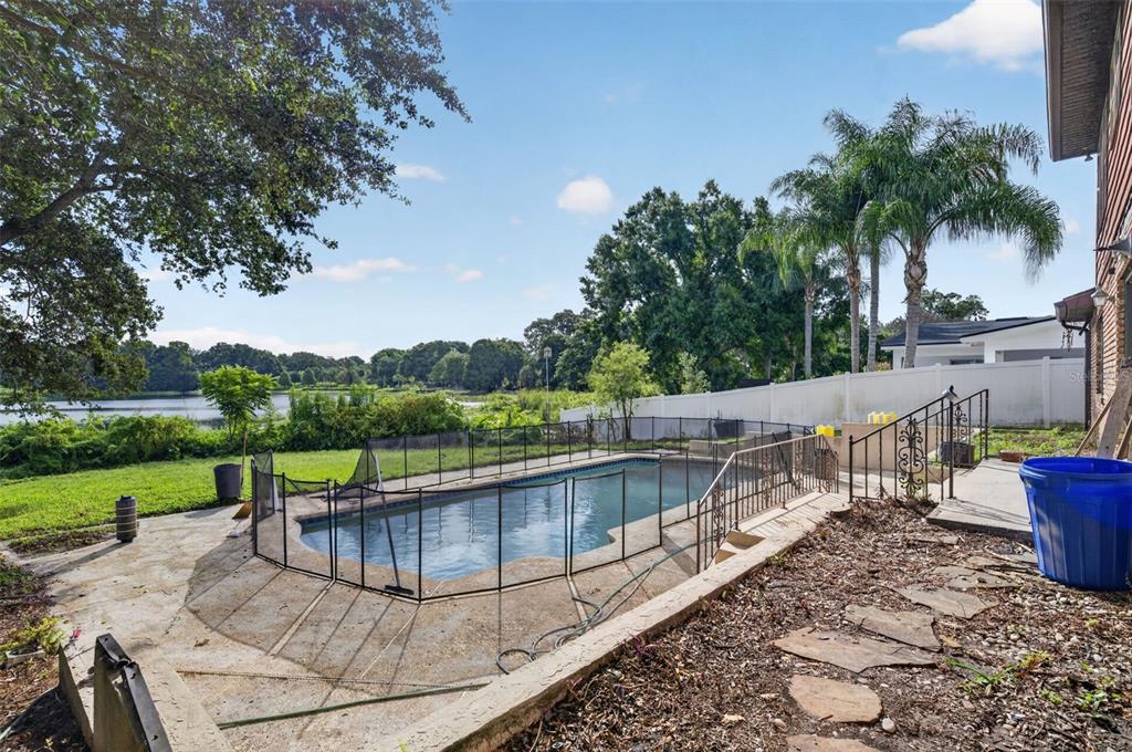 A backyard swimming pool with a safety fence overlooks a lake and green trees — 3513 MARWOOD DRIVE, ORLANDO, FL