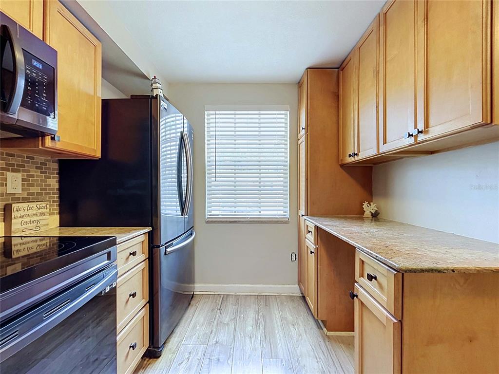 A kitchen features wood cabinets, granite countertops, a black refrigerator, and a window with blinds — 4227 SHELDON PLACE UNIT -, NEW PORT RICHEY, FL