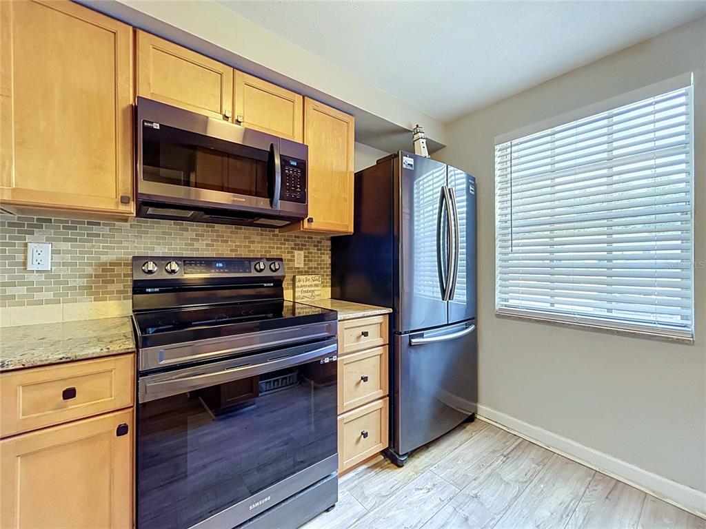 A kitchen features light wood cabinets, stainless steel appliances, a tiled backsplash, and a window — 4227 SHELDON PLACE UNIT -, NEW PORT RICHEY, FL