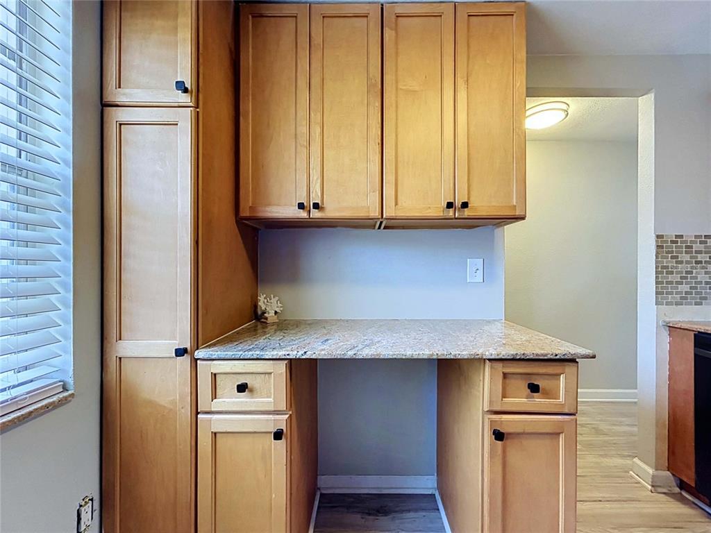 A kitchen desk area features light wood cabinets, granite countertops, and a tiled backsplash — 4227 SHELDON PLACE UNIT -, NEW PORT RICHEY, FL