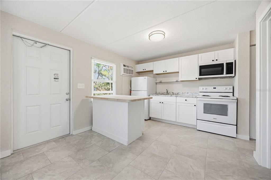 A kitchen with white cabinets, white appliances, a small island, and light-colored tile flooring — 419 GRAPEFRUIT AVENUE UNIT 8B, SEBRING, FL