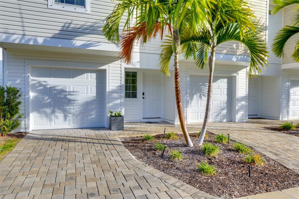 A white townhouse exterior features a garage, a front door, and a small palm tree — 2441 6TH AVENUE DRIVE E, BRADENTON, FL