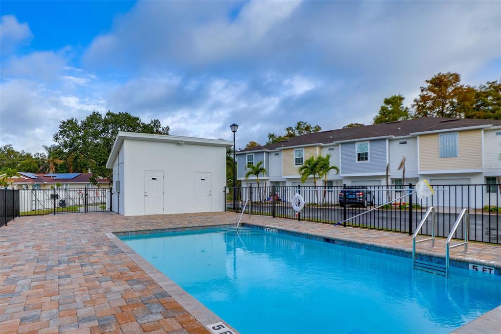 A rectangular swimming pool sits in front of a white utility building and townhomes — 2441 6TH AVENUE DRIVE E, BRADENTON, FL