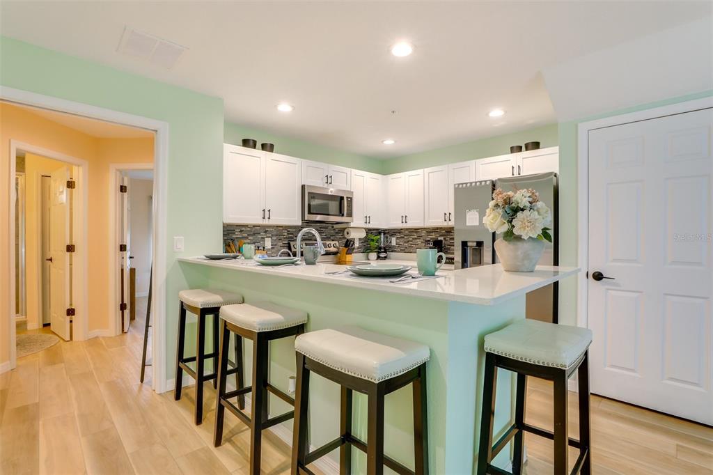 A kitchen features white cabinets, a light green island with bar stools, and stainless appliances — 2441 6TH AVENUE DRIVE E, BRADENTON, FL