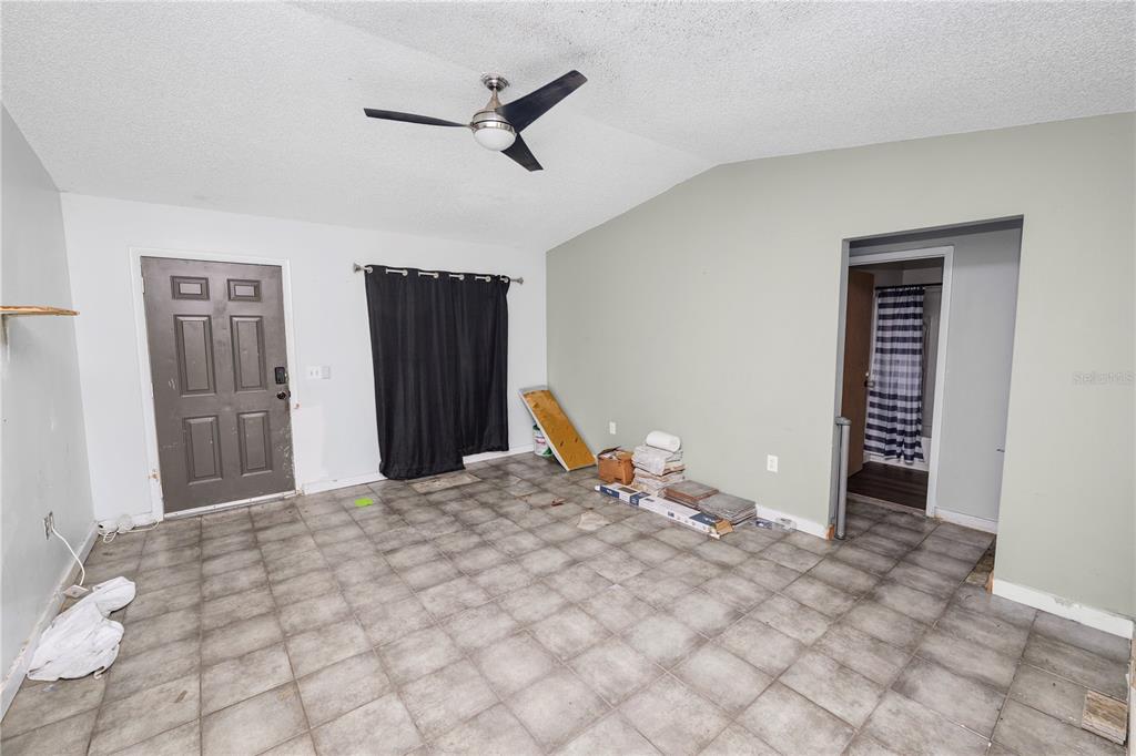 An empty room features gray tile flooring, a vaulted ceiling with a fan, and a door — 136 MADERA DRIVE, WINTER HAVEN, FL