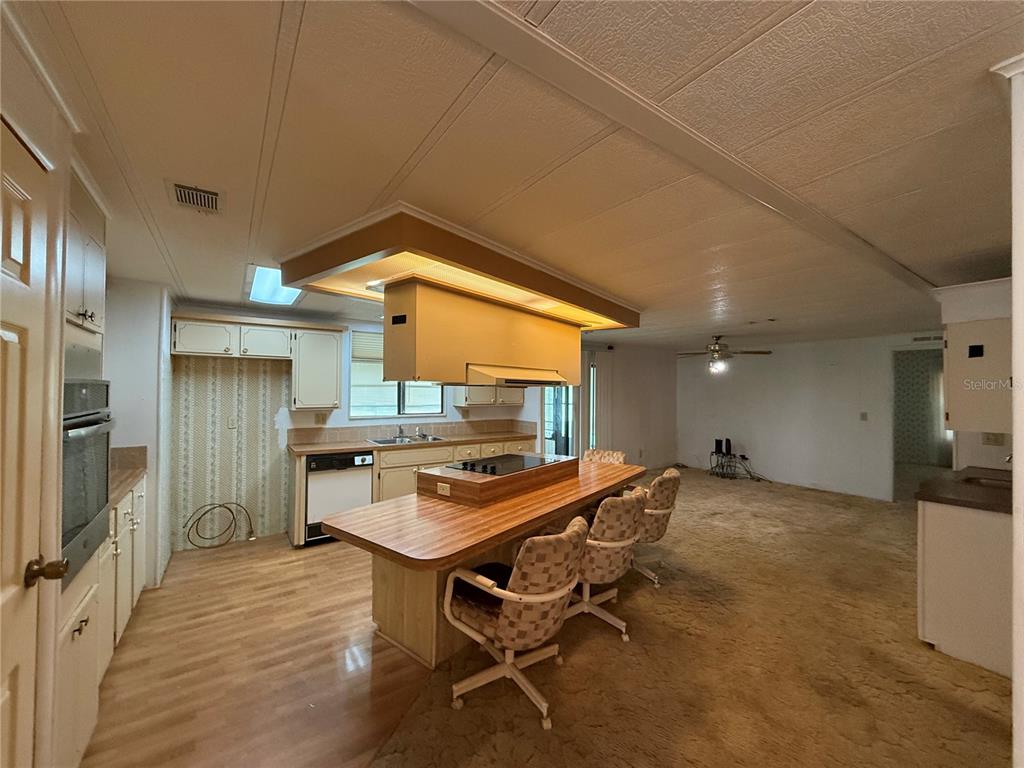 A kitchen with a central island and cooktop opens into a carpeted living area — 4 GROVE COURT, WILDWOOD, FL