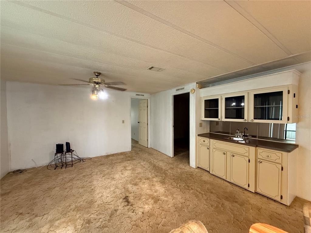 A living area with beige carpet, a ceiling fan, and a small kitchenette with cabinets — 4 GROVE COURT, WILDWOOD, FL