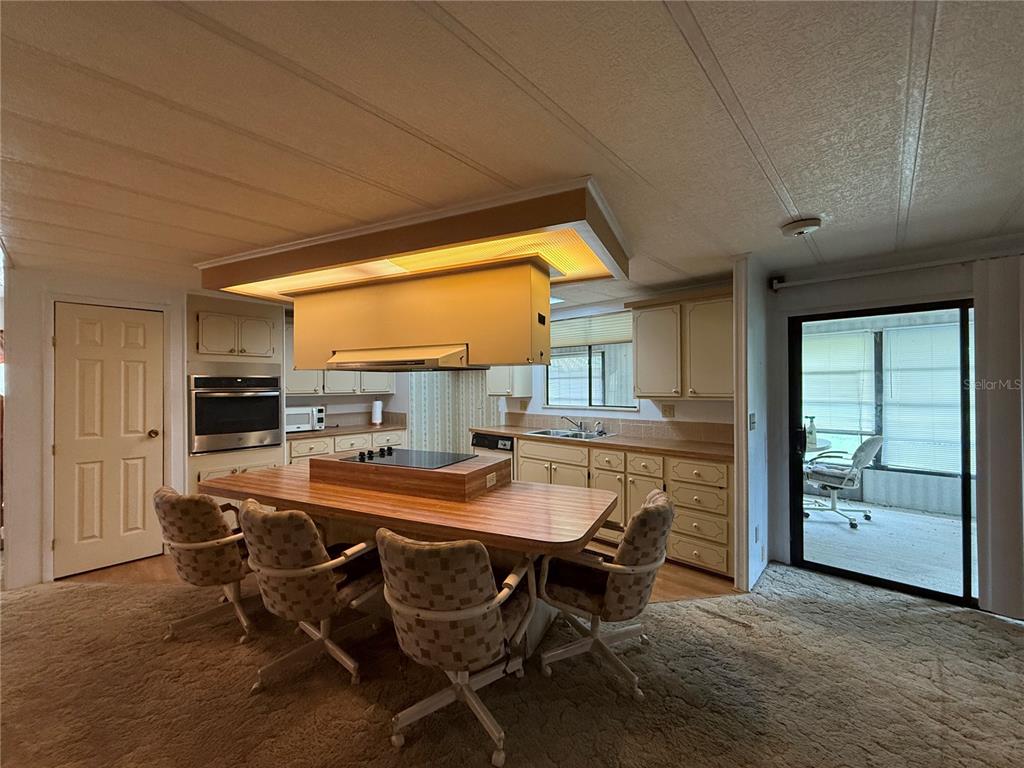 A kitchen features a central island with a cooktop, wood cabinetry, and carpeted flooring — 4 GROVE COURT, WILDWOOD, FL