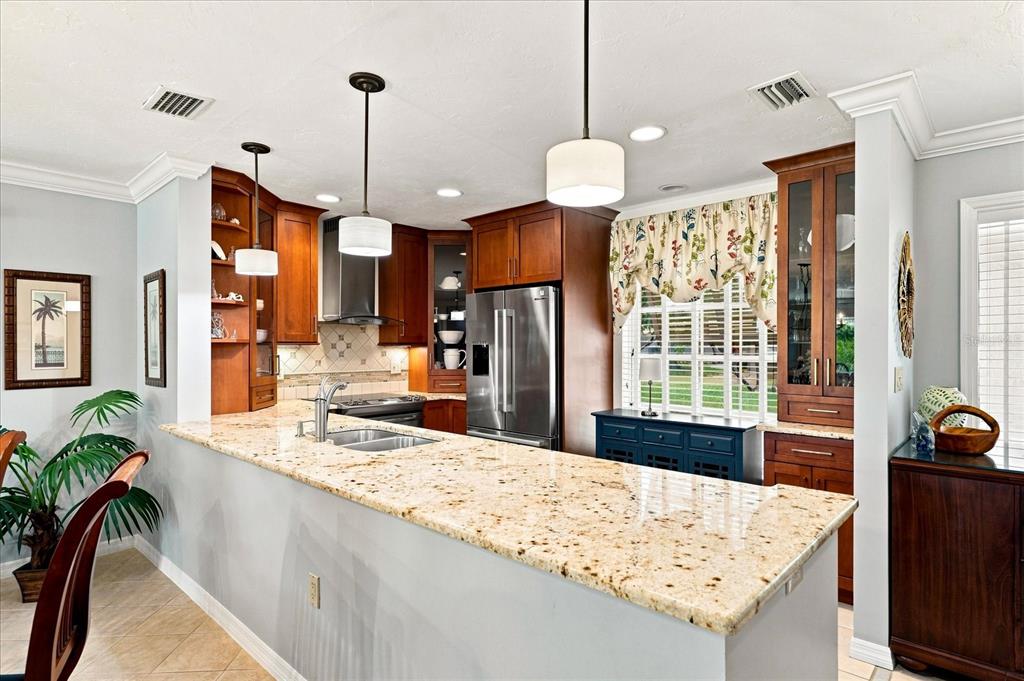 A kitchen features granite countertops, wood cabinetry, stainless steel appliances, and two pendant lights — 3252 RINGWOOD MEADOW UNIT 81, SARASOTA, FL