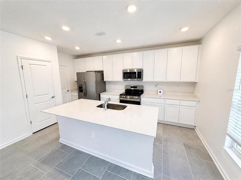 A kitchen features white cabinets, stainless steel appliances, a center island, and gray tile flooring — 832 TIMBERLAND DRIVE, EAGLE LAKE, FL