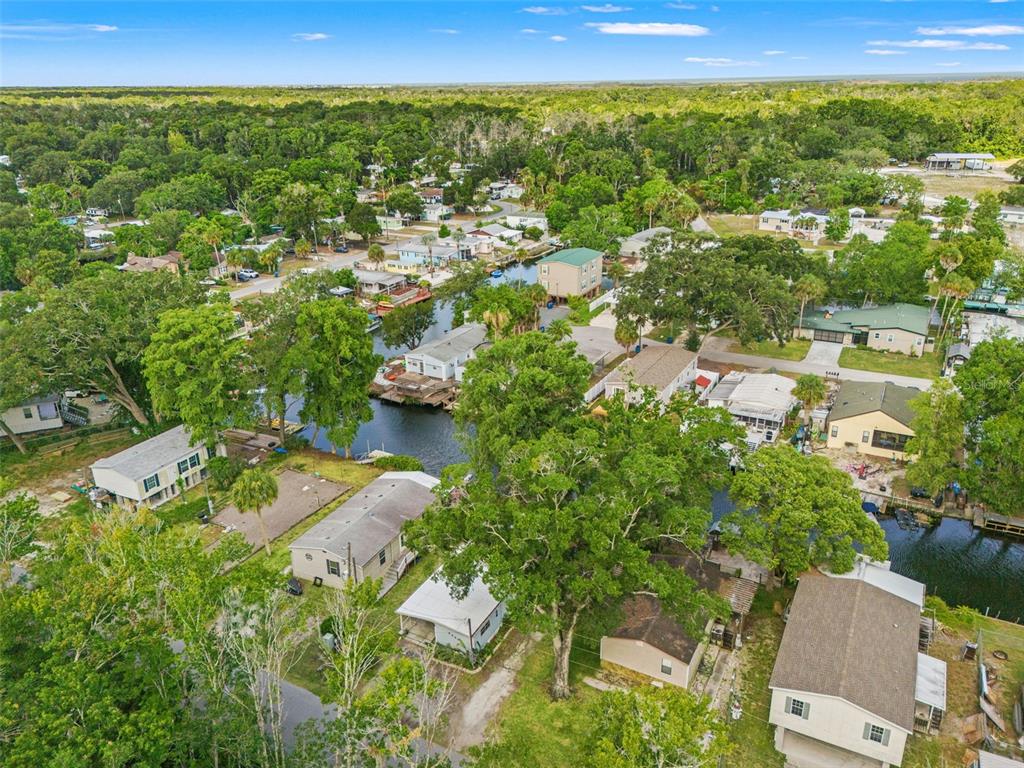 A light blue mobile home with a carport and gravel driveway sits among mature trees — 6380 RICHARD DRIVE, WEEKI WACHEE, FL